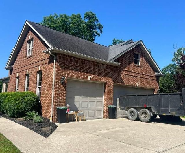Brick house with a two-car garage and a black trailer parked on the driveway on a sunny day