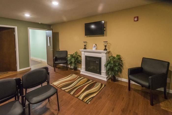 Waiting room with black chairs, fireplace, TV, and decorative plants.