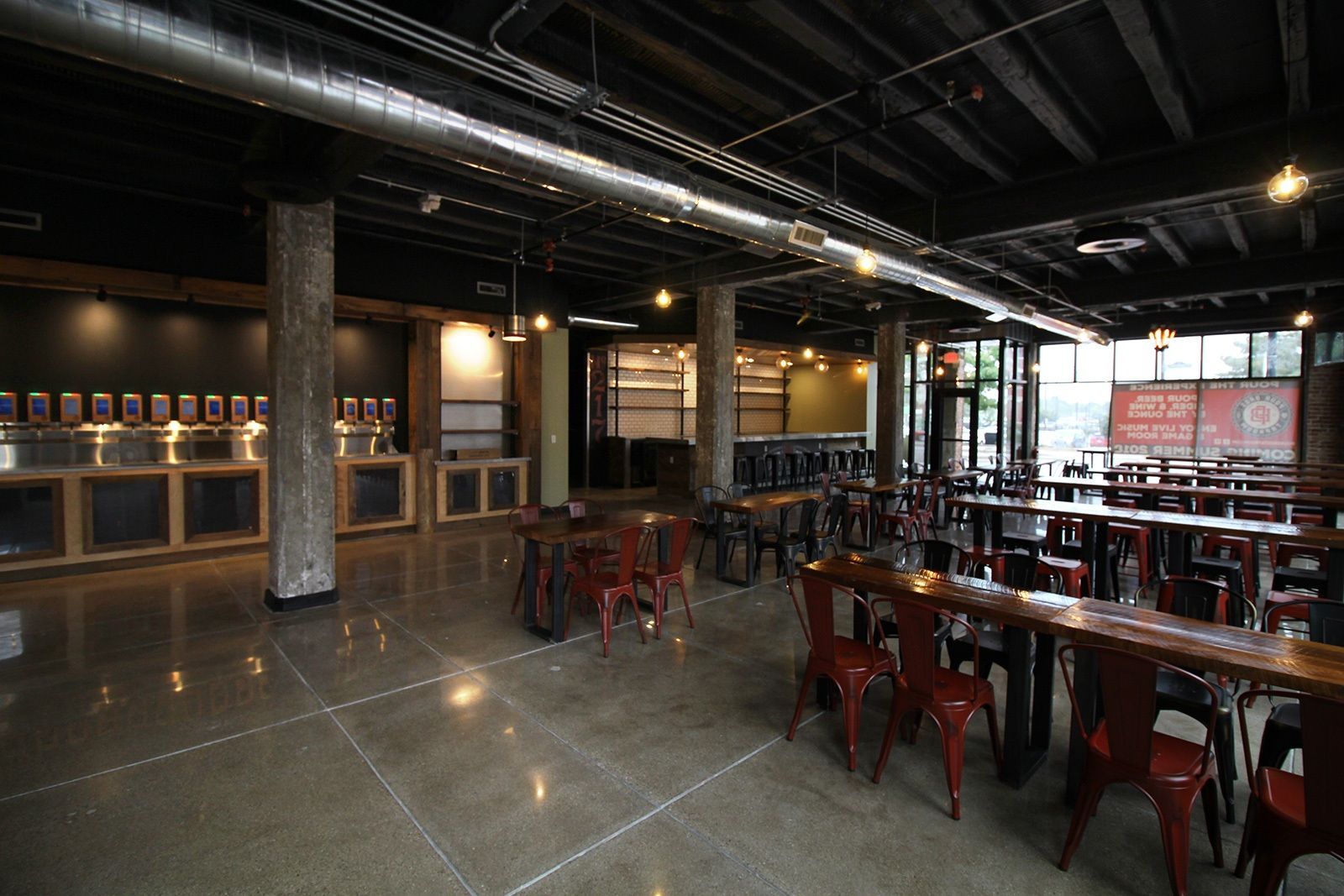 Interior of a modern bar with concrete floors, metal chairs, and beer taps.