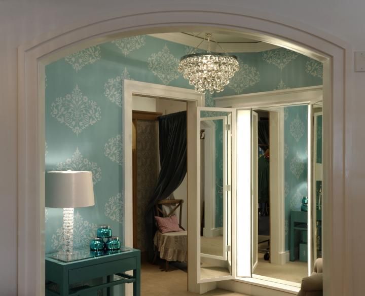 An ornate doorway leads to a room with a chandelier, teal walls, and folding mirrors.