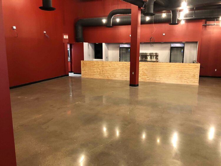 Empty commercial space with red walls, polished concrete floor, and brick-faced counter.