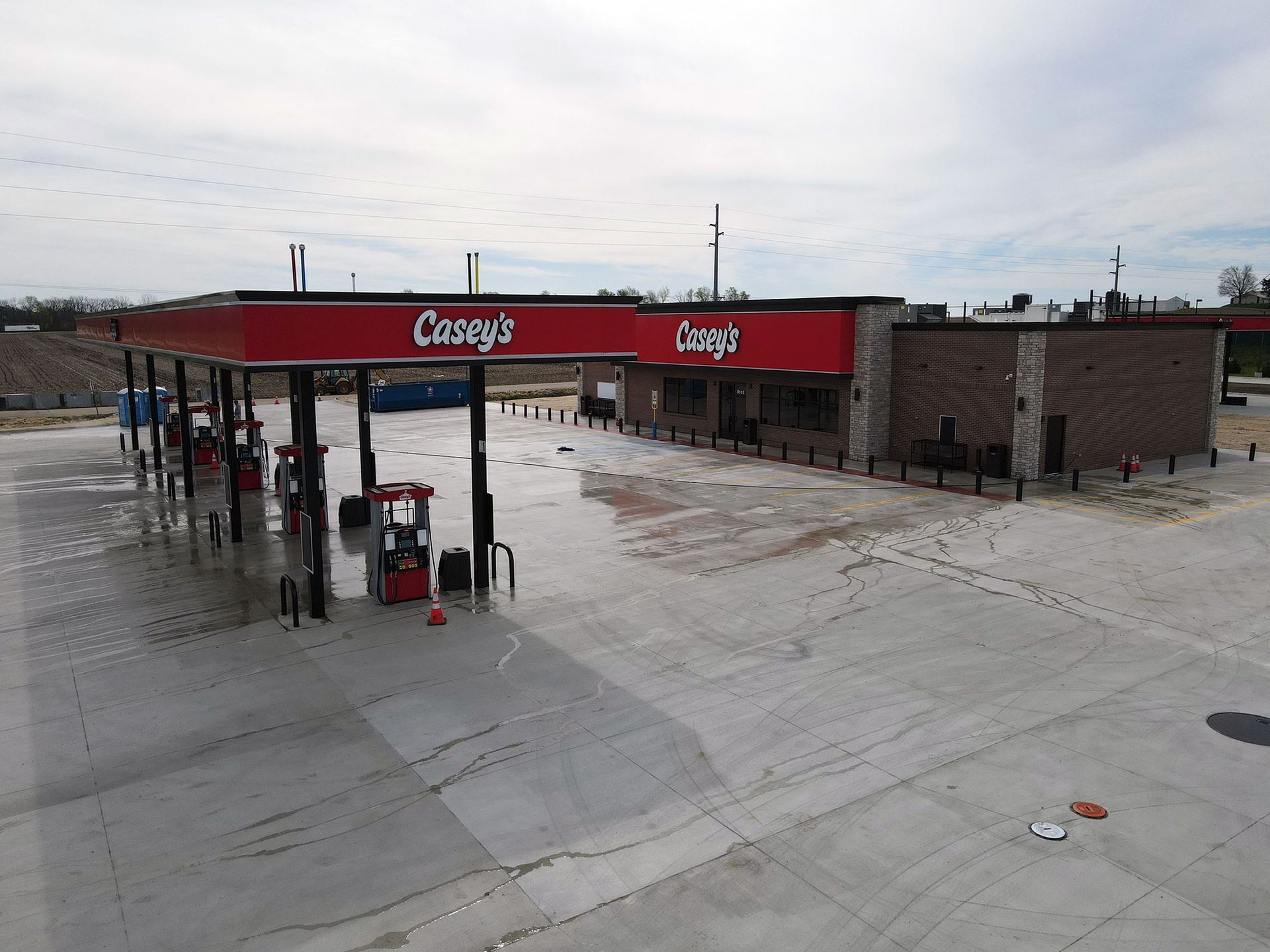 Casey's gas station with red canopy over fuel pumps, adjacent brick building, concrete lot, cloudy sky.