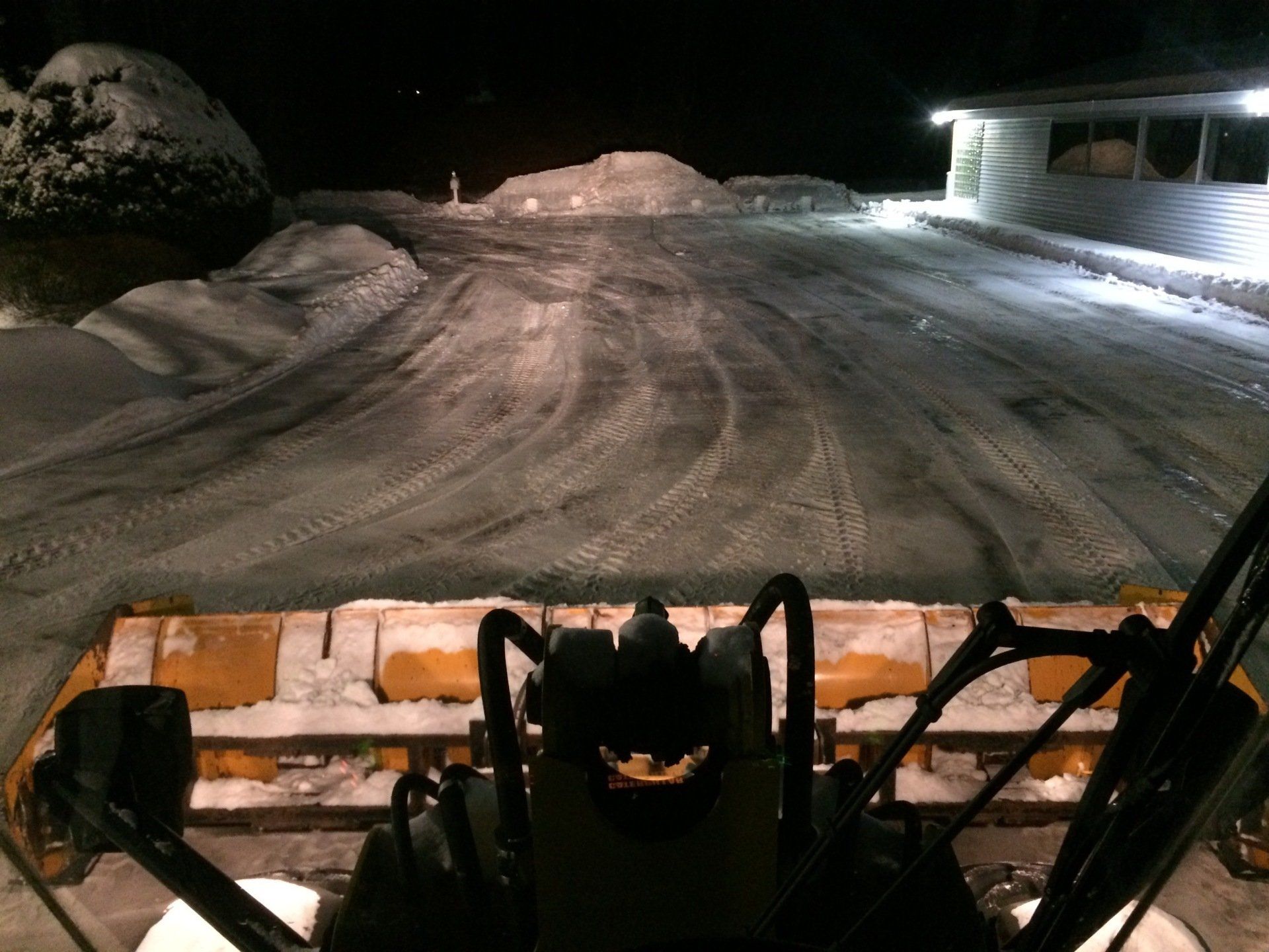 a snow plow is clearing a snowy parking area at night