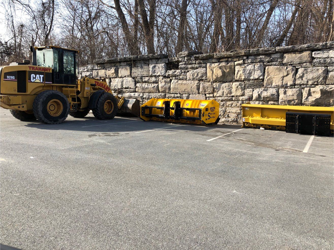 Yellow cat tractor is parked in a parking lot next to a stone wall .