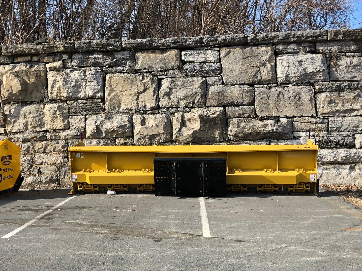 Large yellow plow sitting in front of a stone wall .