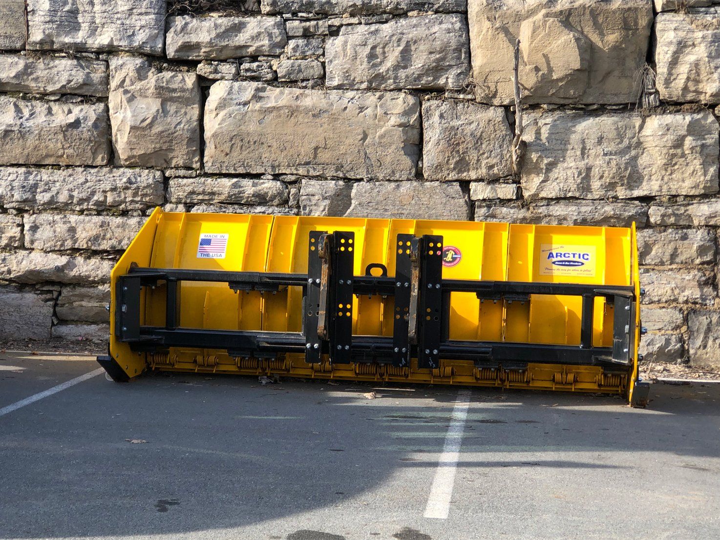 Yellow plow in front of stone wall in parking lot