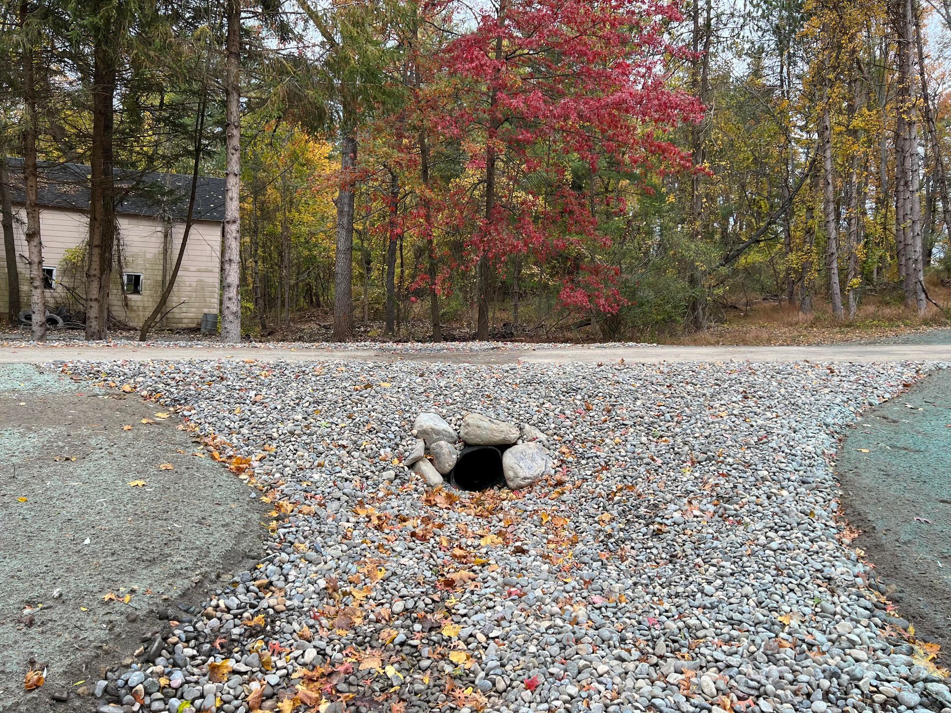 Runoff pipe under a gravel road with trees in the background .