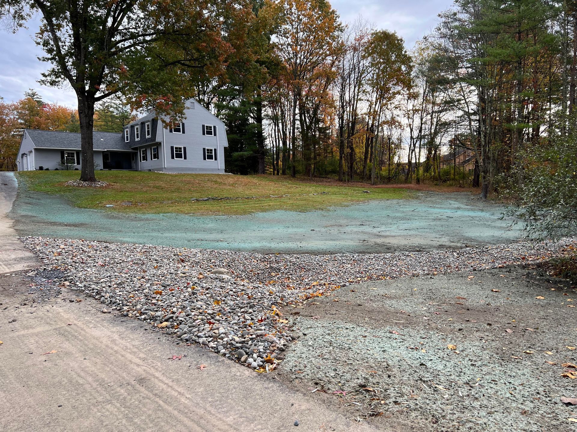 a house with new hydroseeding in the front yard is sitting on top of a hill next to a gravel road.