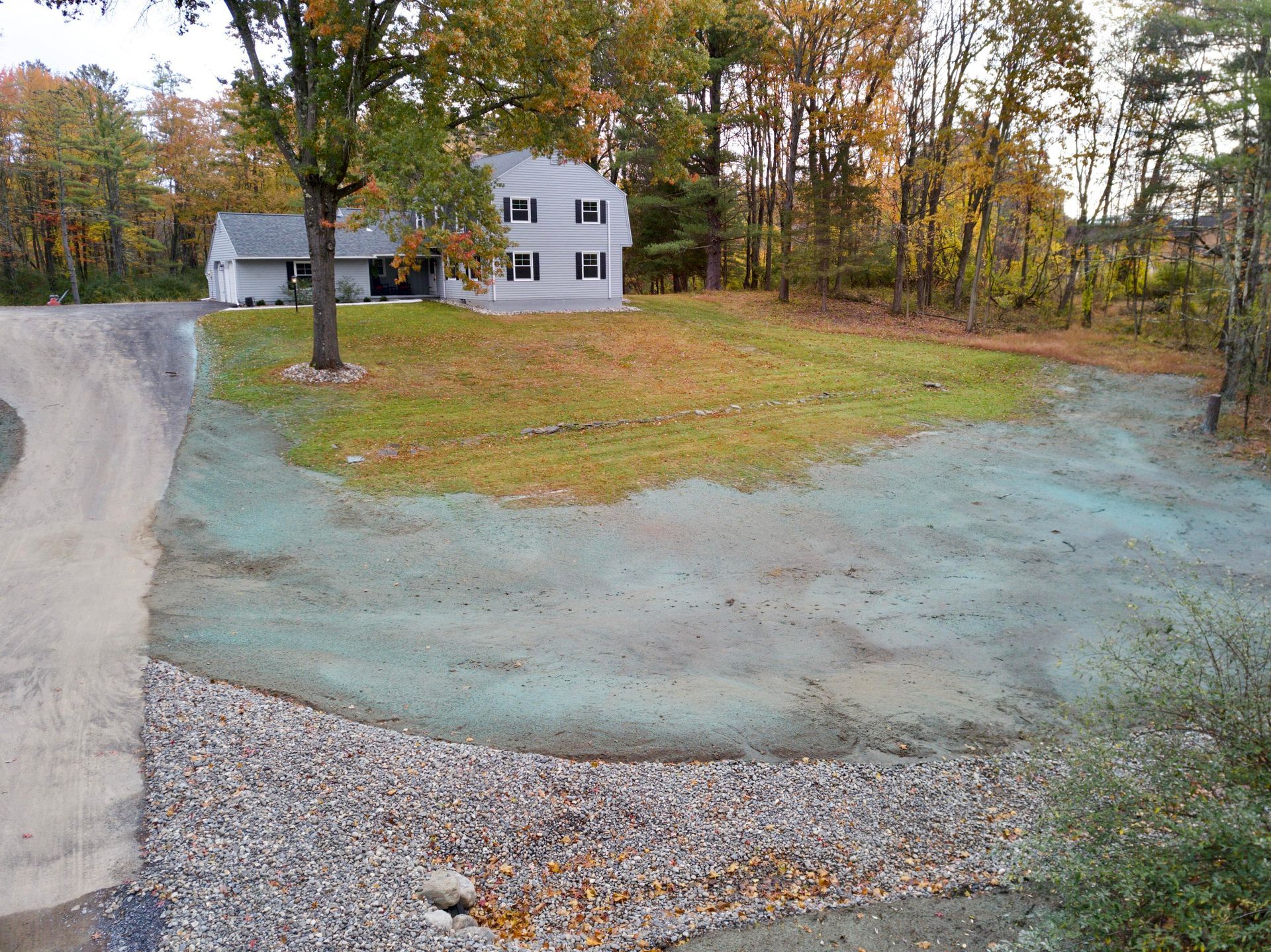 a driveway leading to a house with  new hydroseeding and trees in the background