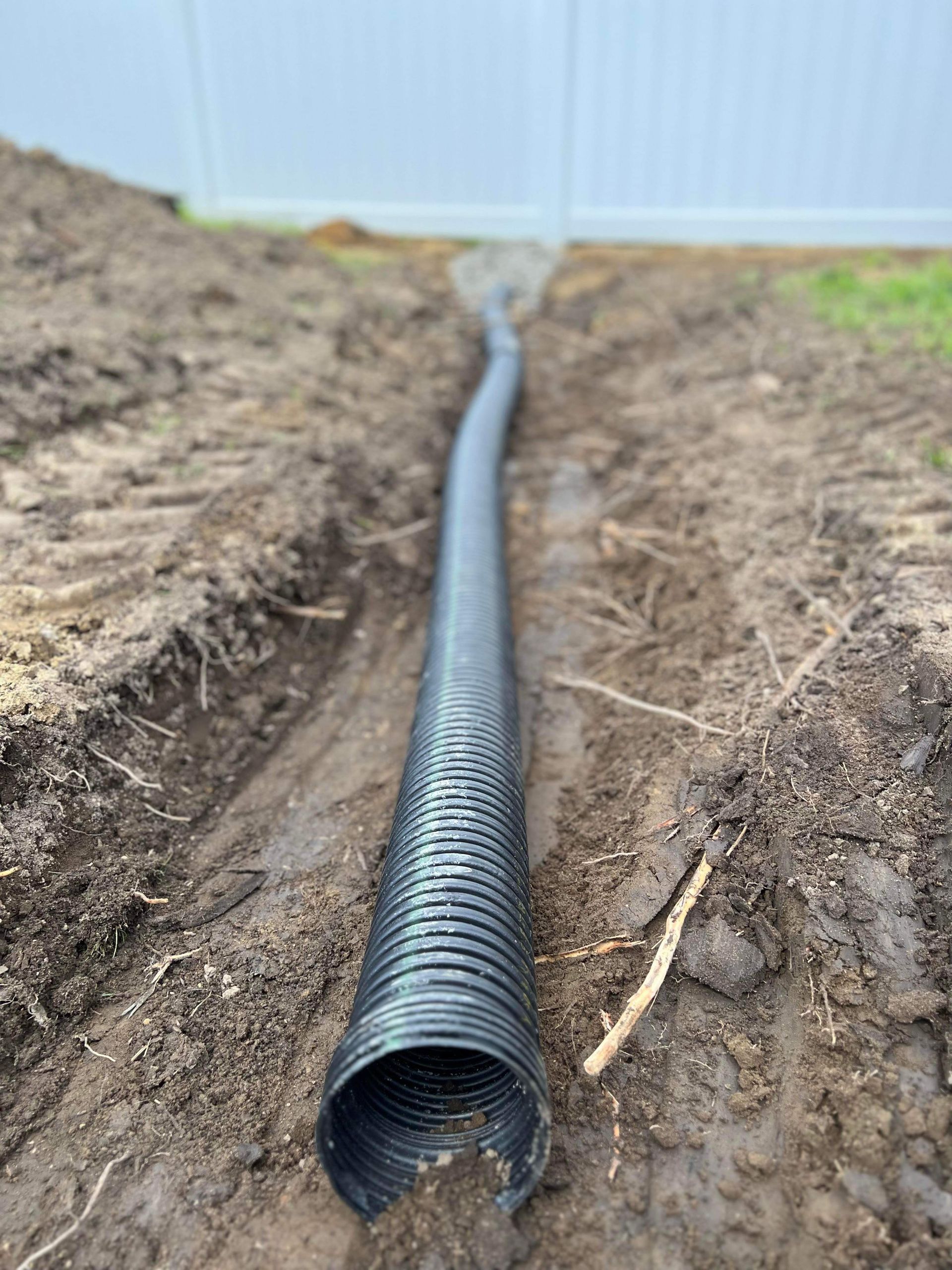 a black pipe is laying in the dirt next to a fence .