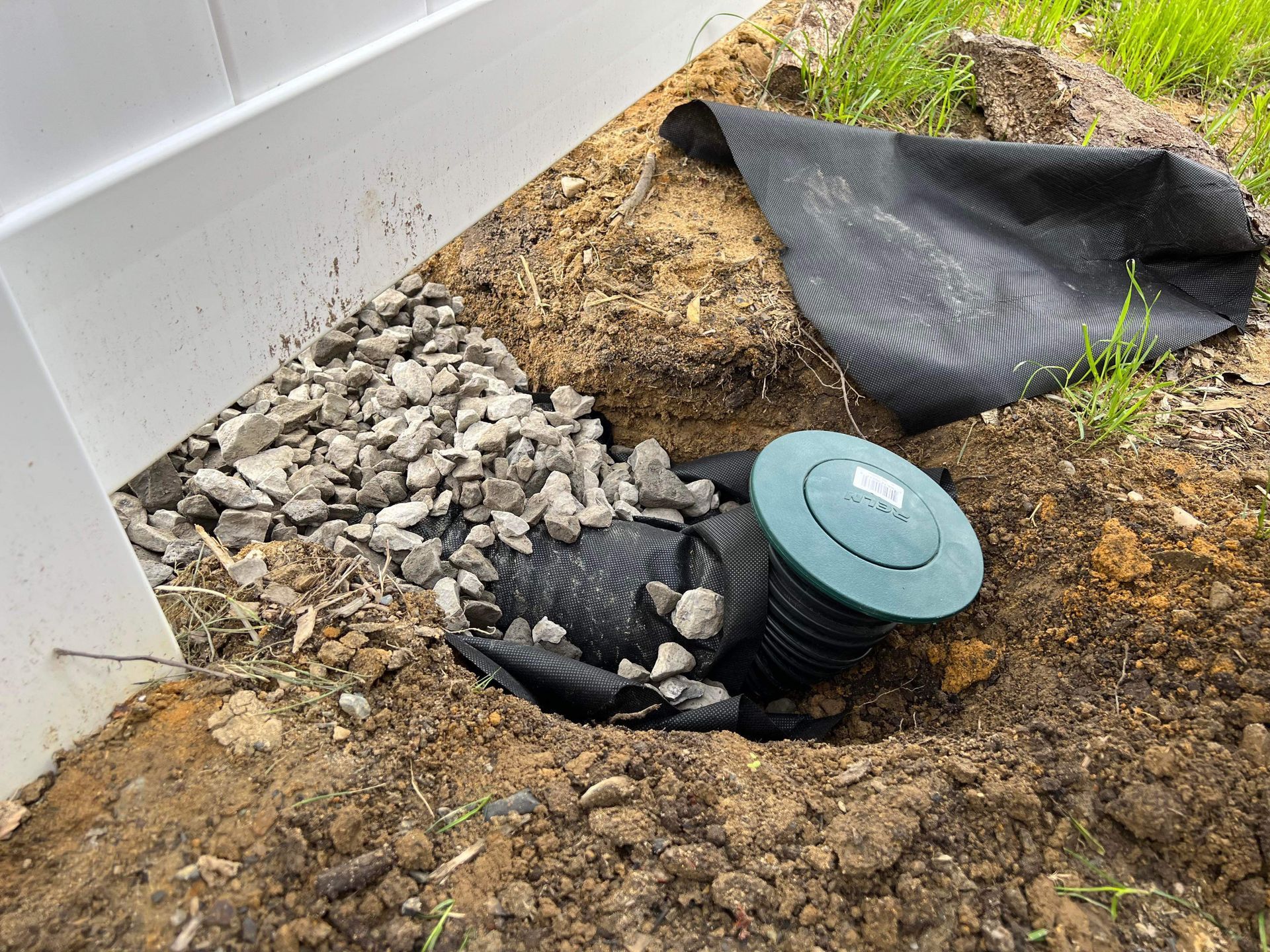 a green pipe is sitting in the dirt next to a fence .