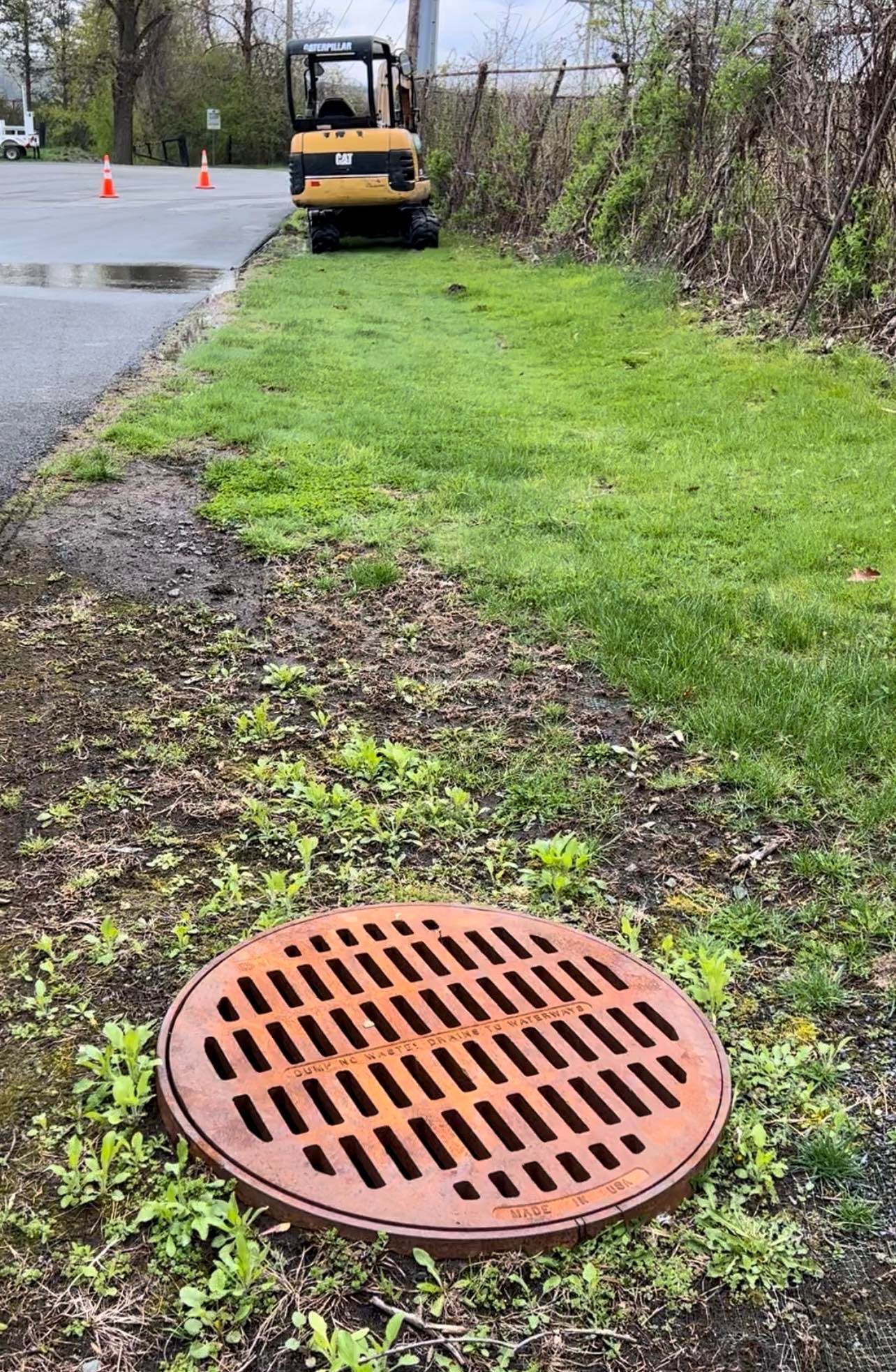 a manhole cover is sitting on the side of the road next to an excavator .