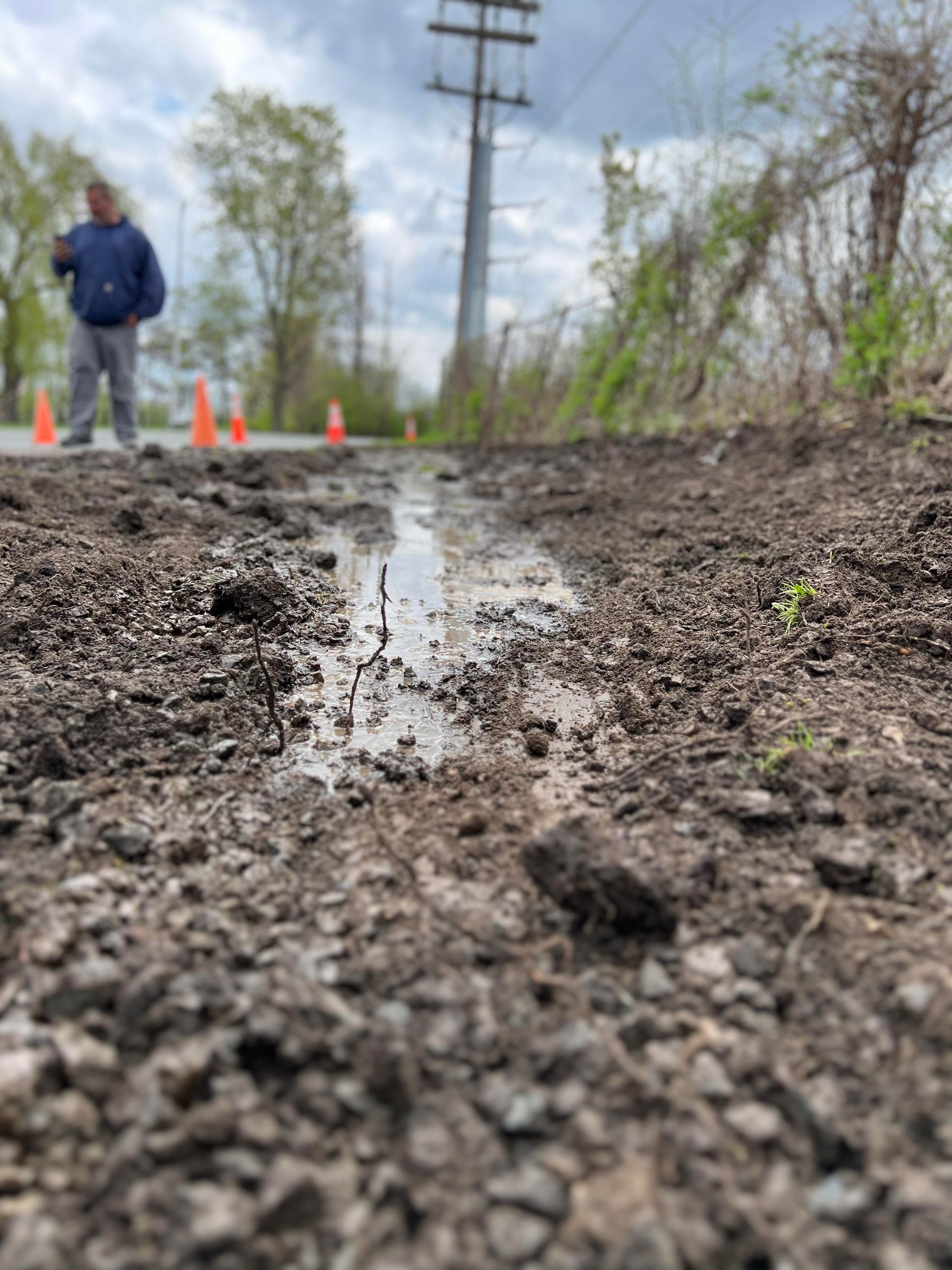 a man is standing on a muddy road next to a shallow trench .