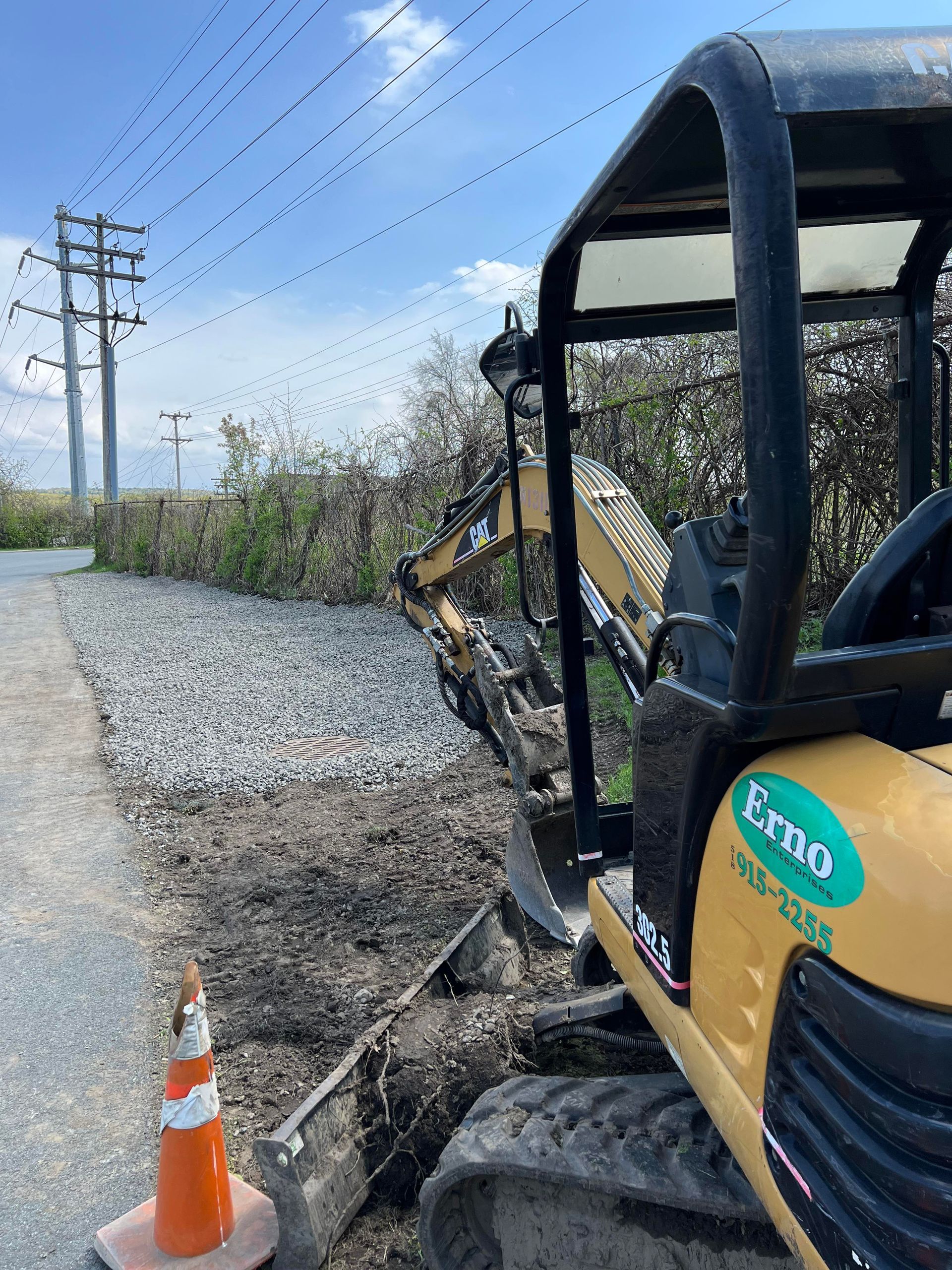 a yellow excavator is sitting on the side of a road next to a plastic cone .