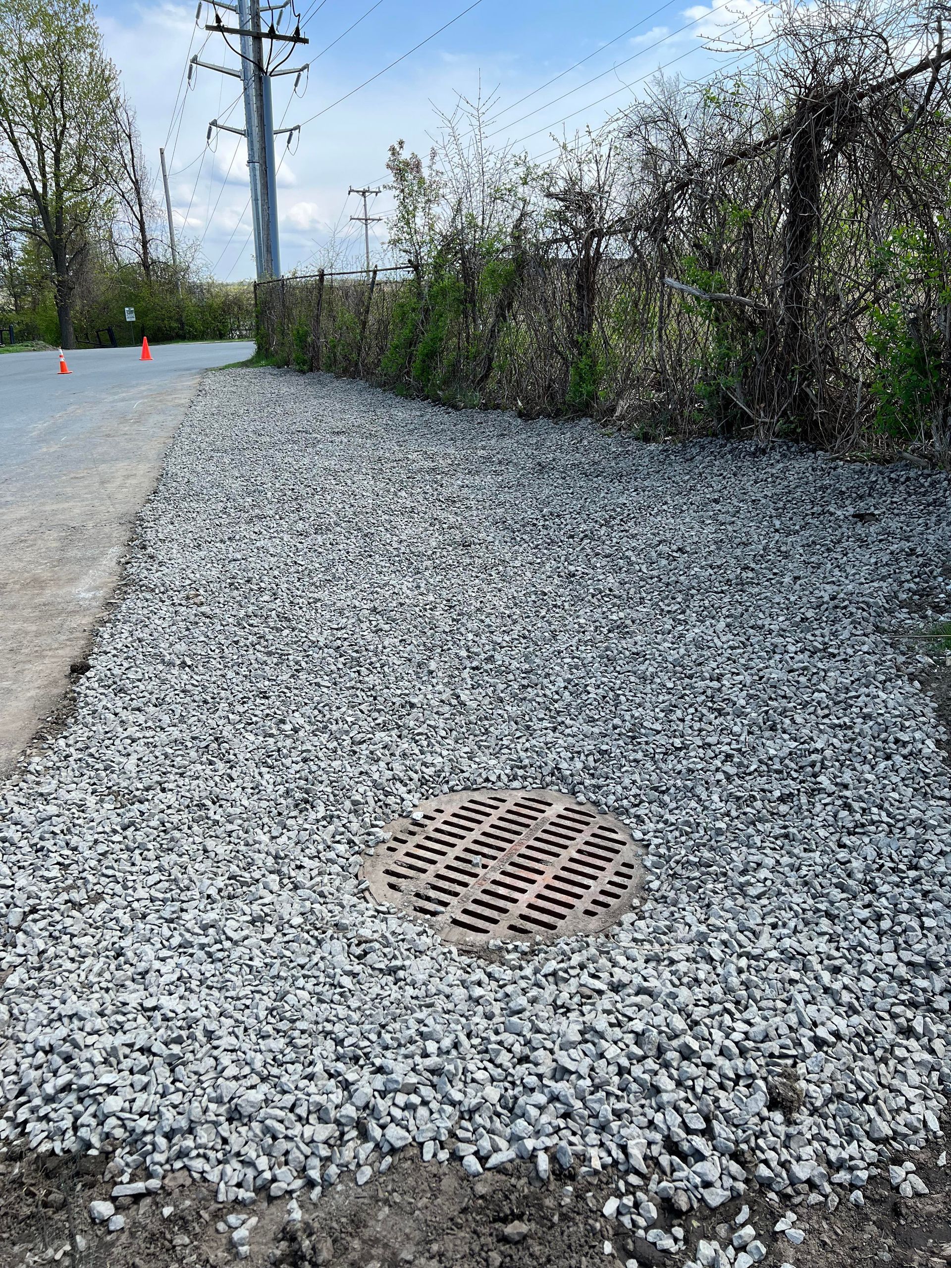 a manhole cover is sitting on top of a pile of gravel next to a road .