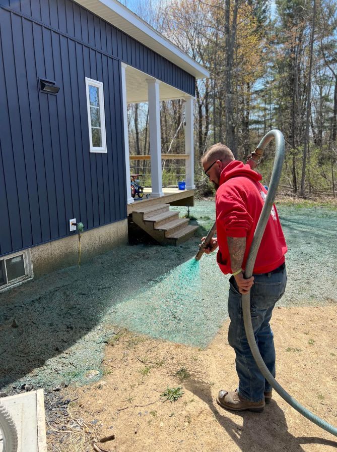 a worker is spraying hydroseeding material with a hose in front of a house .
