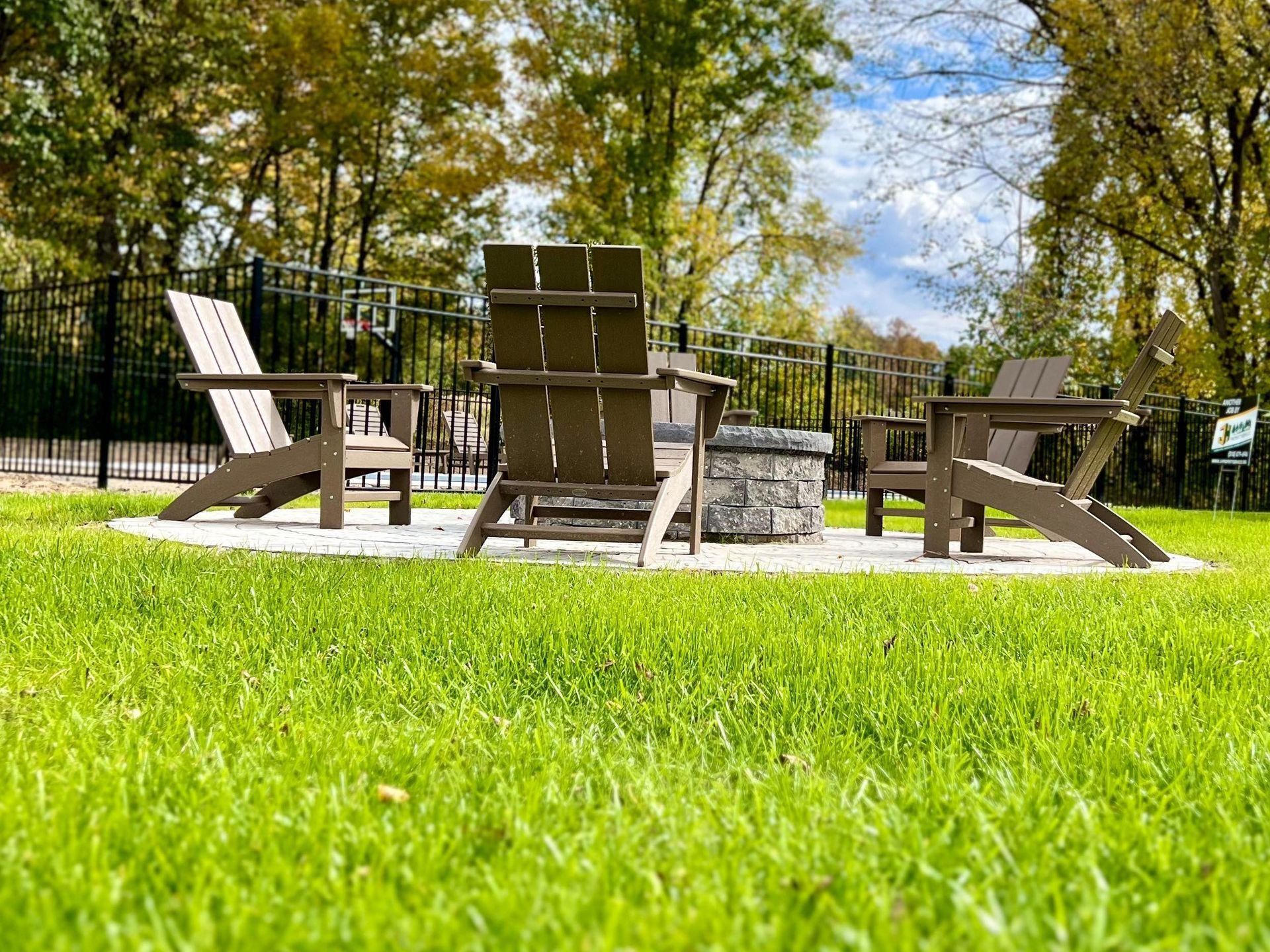 a group of chairs are sitting around a fire pit in the middle of a lush green yard .