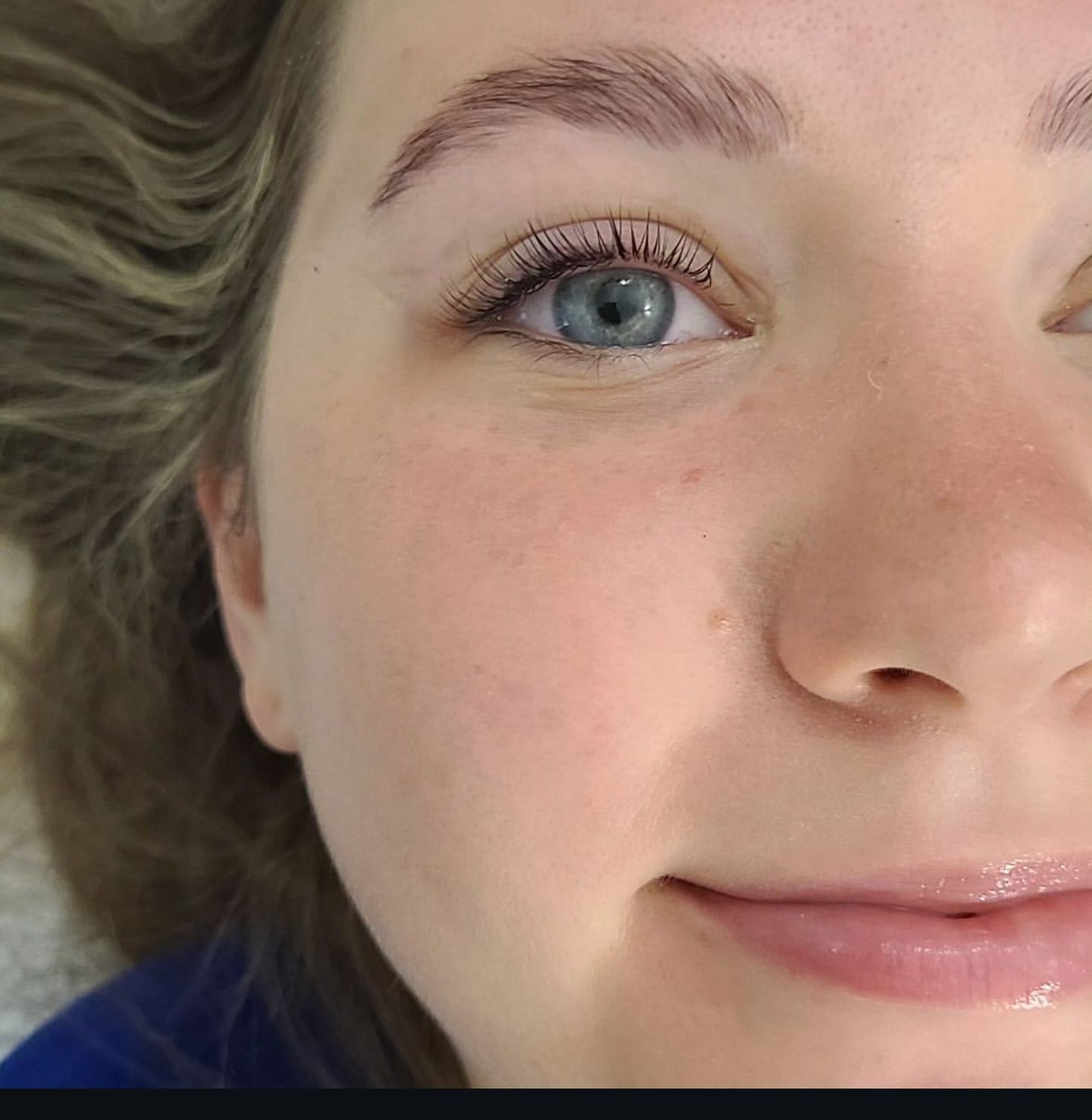 Woman with light skin, blue eyes, and light brown eyebrows smiling.