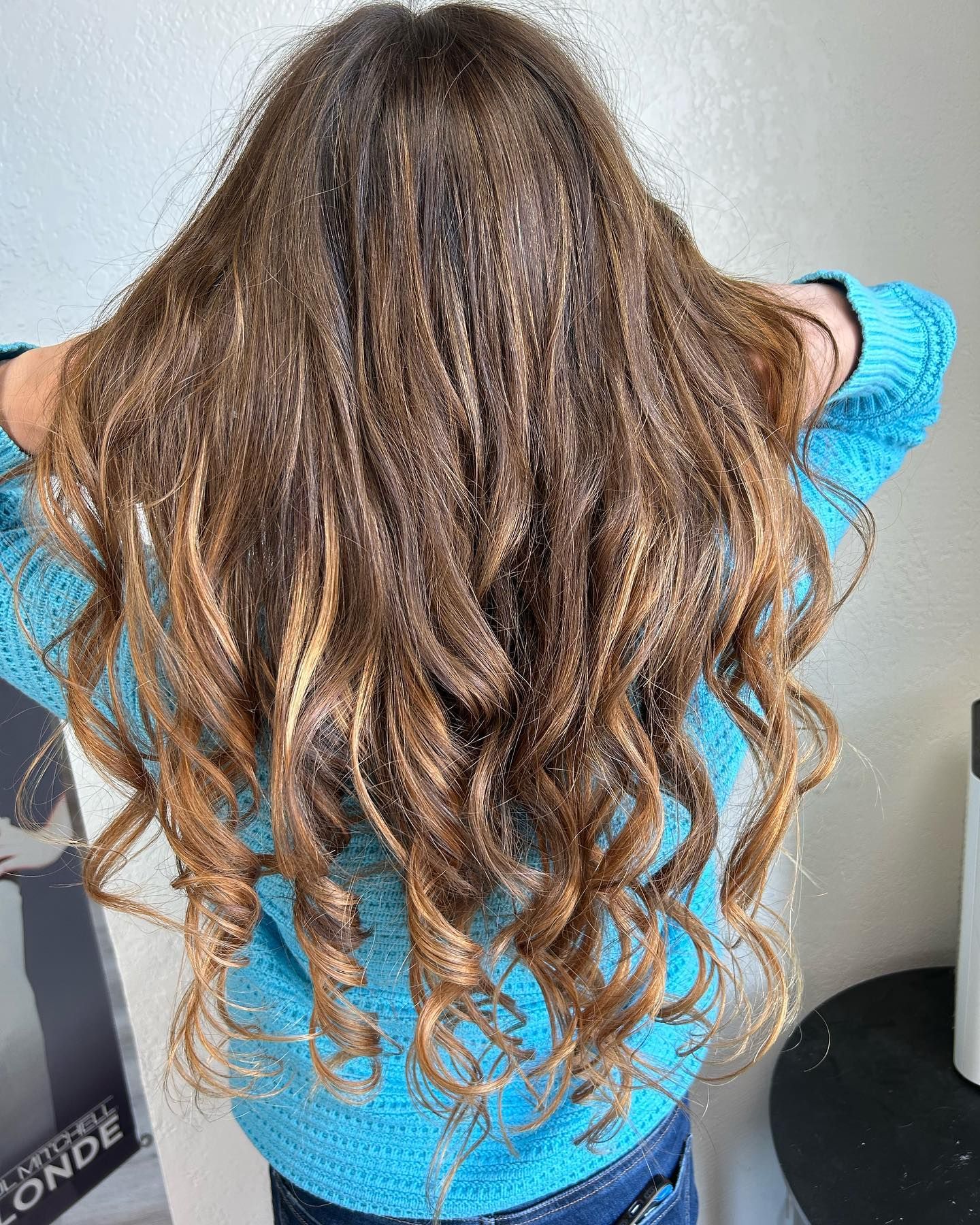 Long, wavy brown hair with blonde highlights; person wearing a blue sweater.