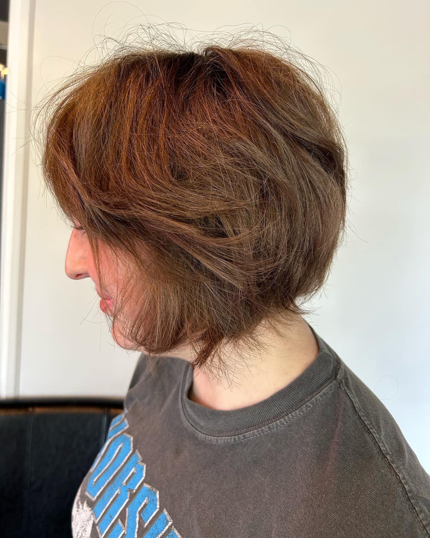 Person with brown, layered bob haircut, wearing a gray t-shirt.