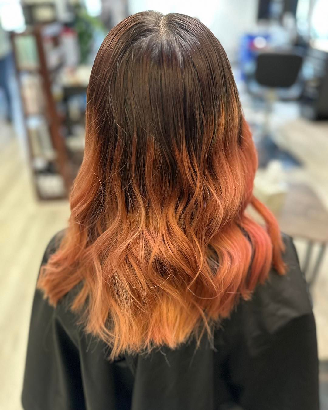 Woman with brown to peach ombre hair. Wavy, shoulder-length style in a salon setting.