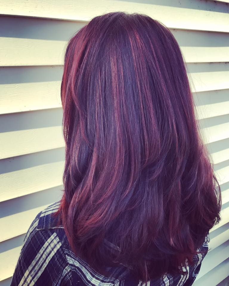 Woman's hair, auburn and layered, with strands of reddish highlights, against a light-colored wood wall.