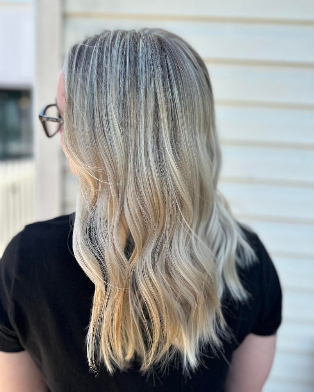 Blonde wavy hair, gradient color. Person wearing a black shirt, standing in front of a white wall.