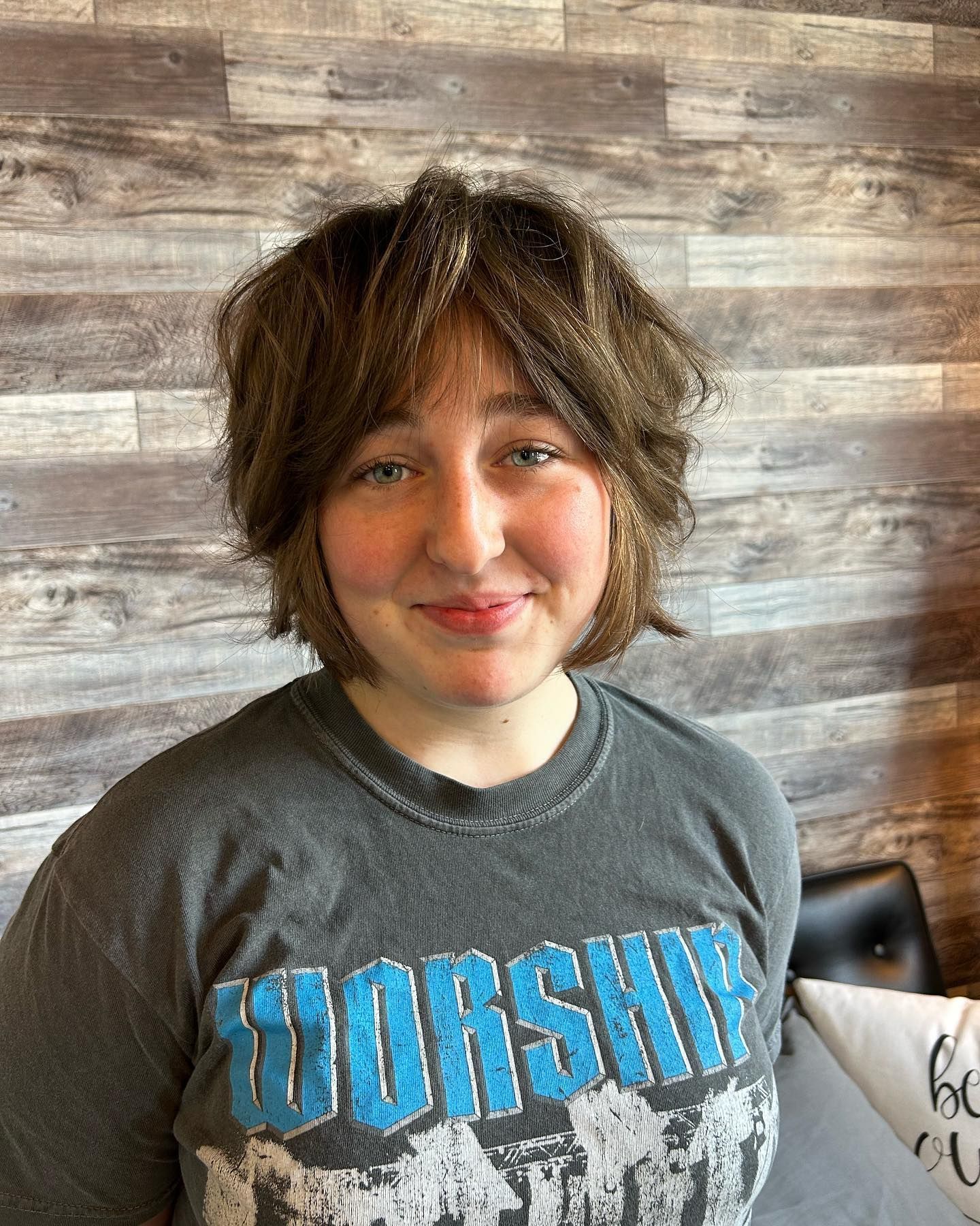 Person with short brown hair smiles, wearing a gray t-shirt with 