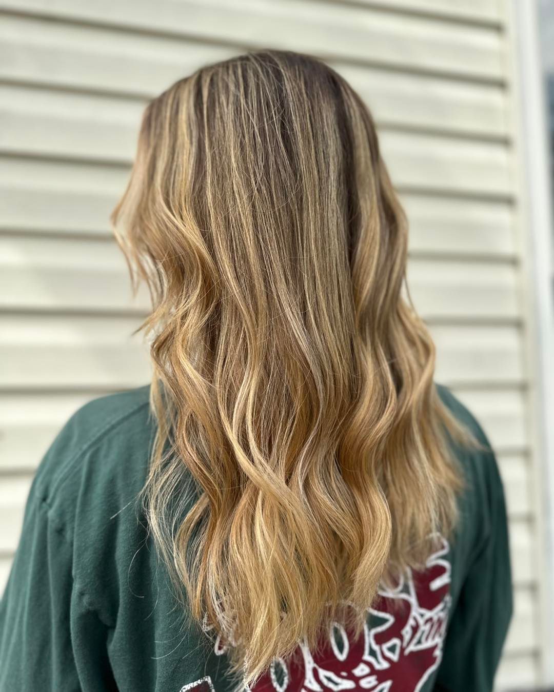 Woman with long, wavy blonde hair with highlights, wearing a green sweatshirt.