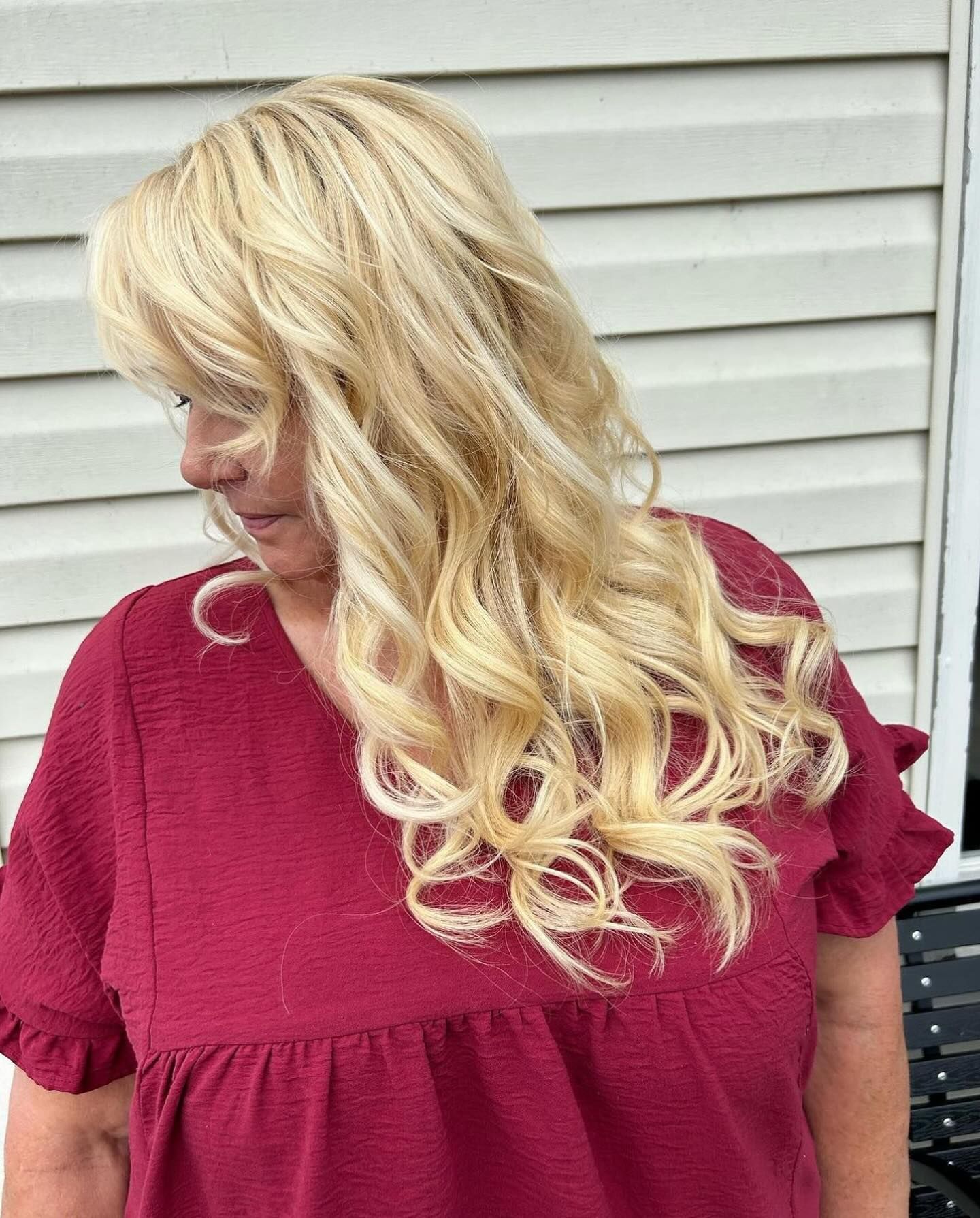 Woman with blonde, wavy hair wearing a maroon top, looking down.