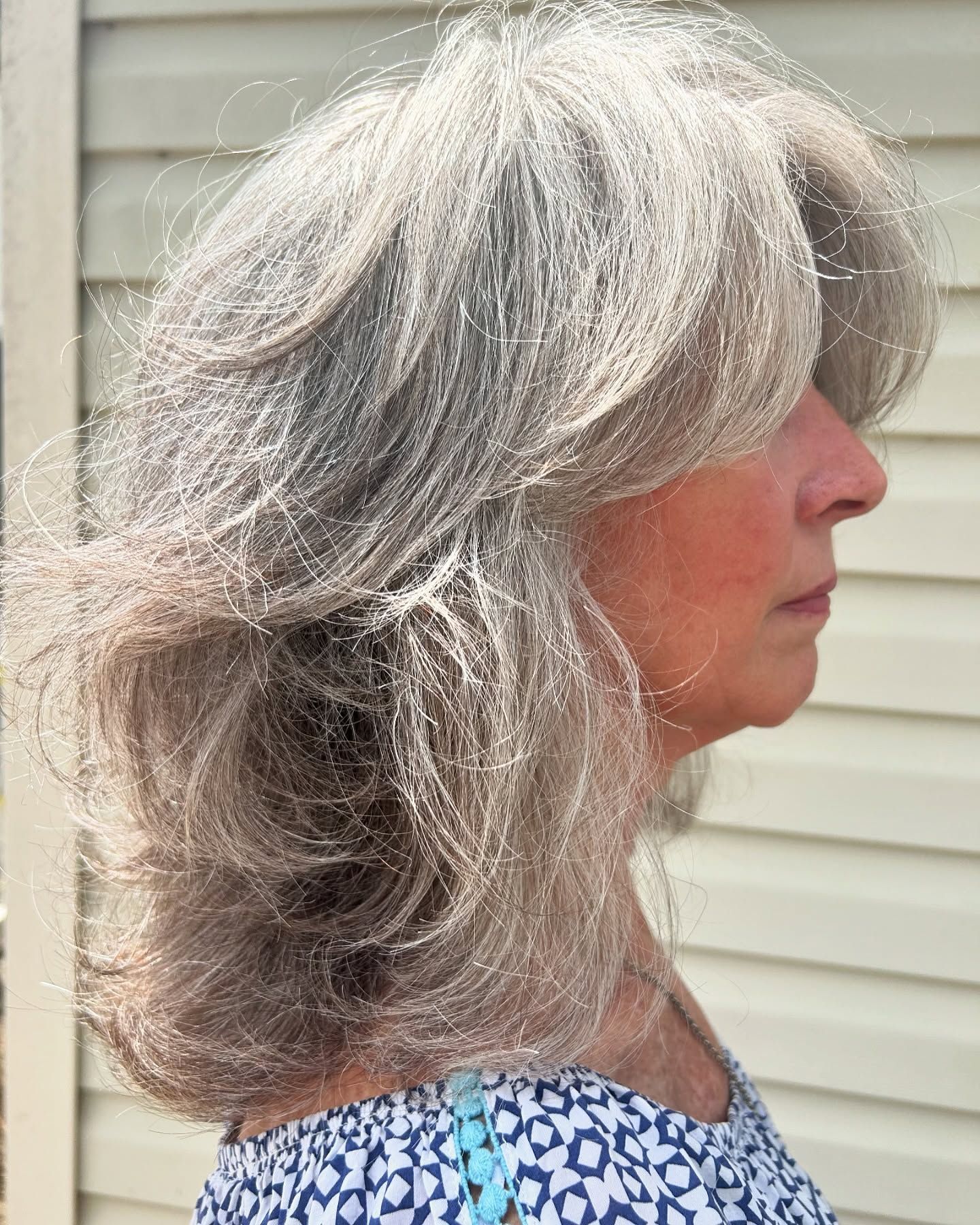Woman with layered gray hair, profile view, wearing a patterned top, outdoors.
