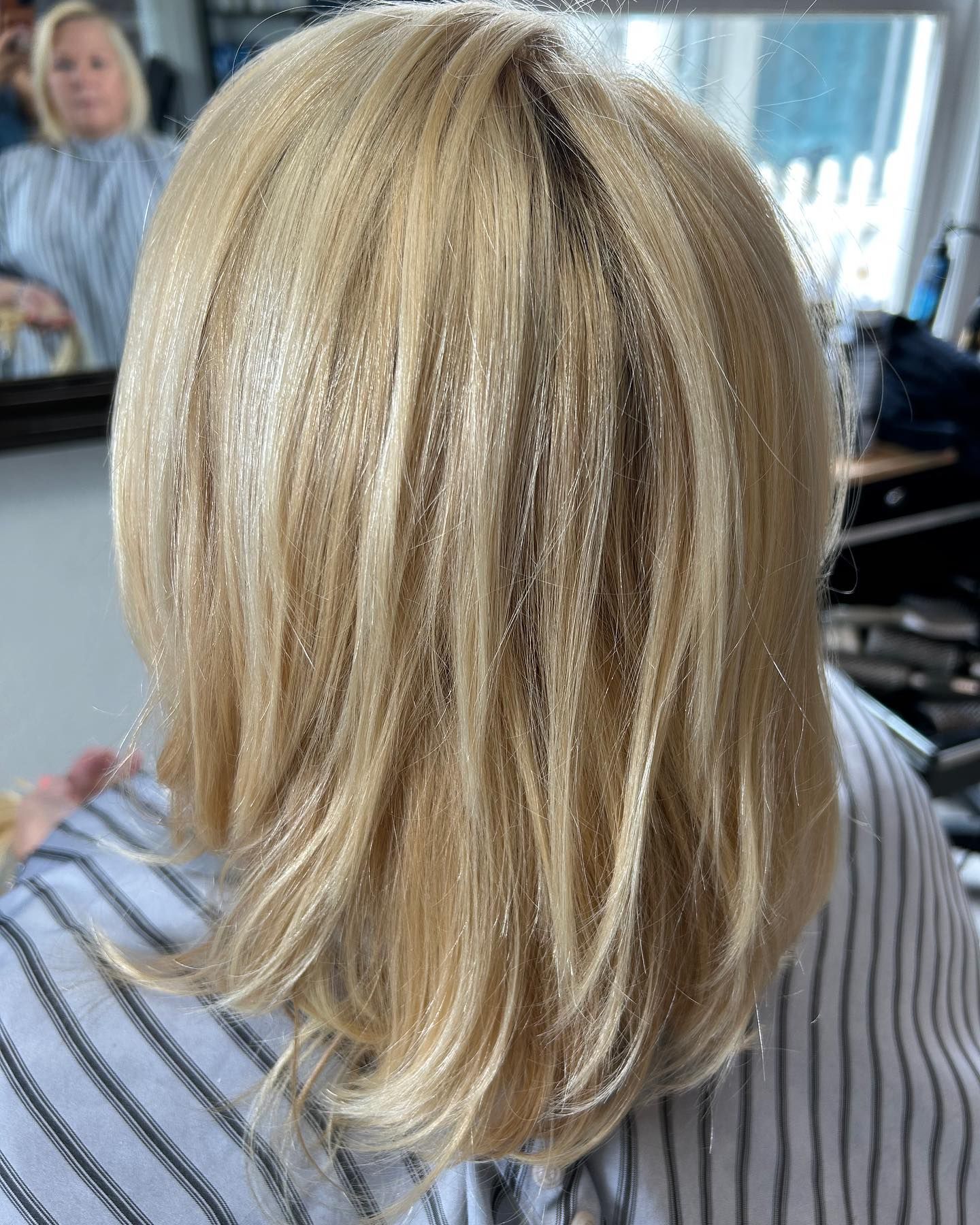 Blonde hair, styled in a bob, with glitter. In a salon, wearing striped cape.