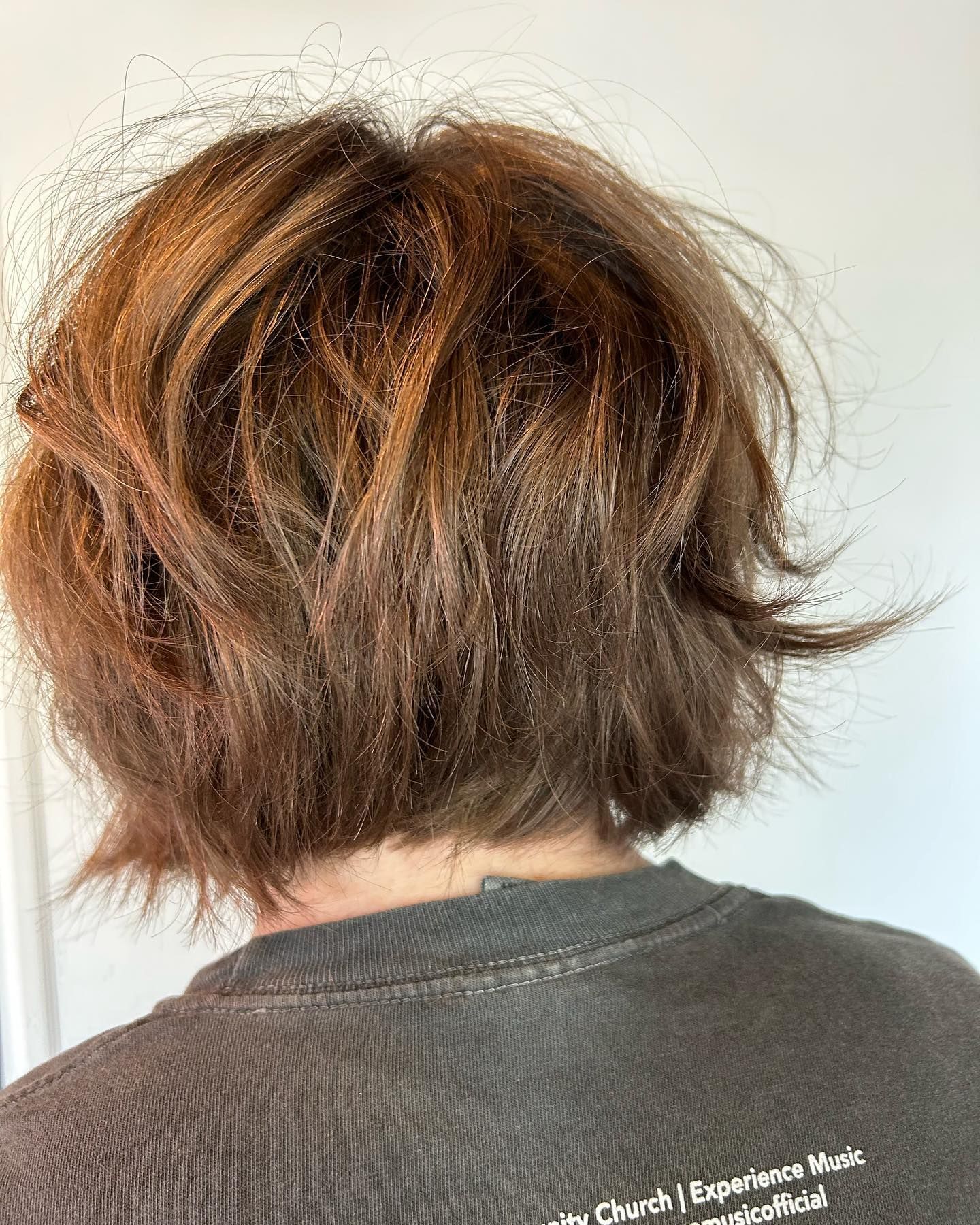 Back view of a person with messy, layered brown hair, cut at the nape of the neck, and wearing a dark gray shirt.