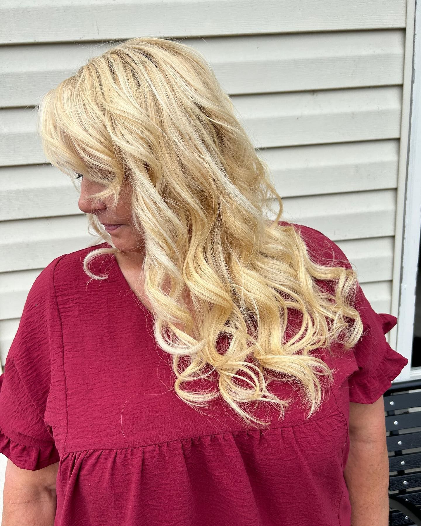 Woman with blonde wavy hair wearing a burgundy blouse outdoors.