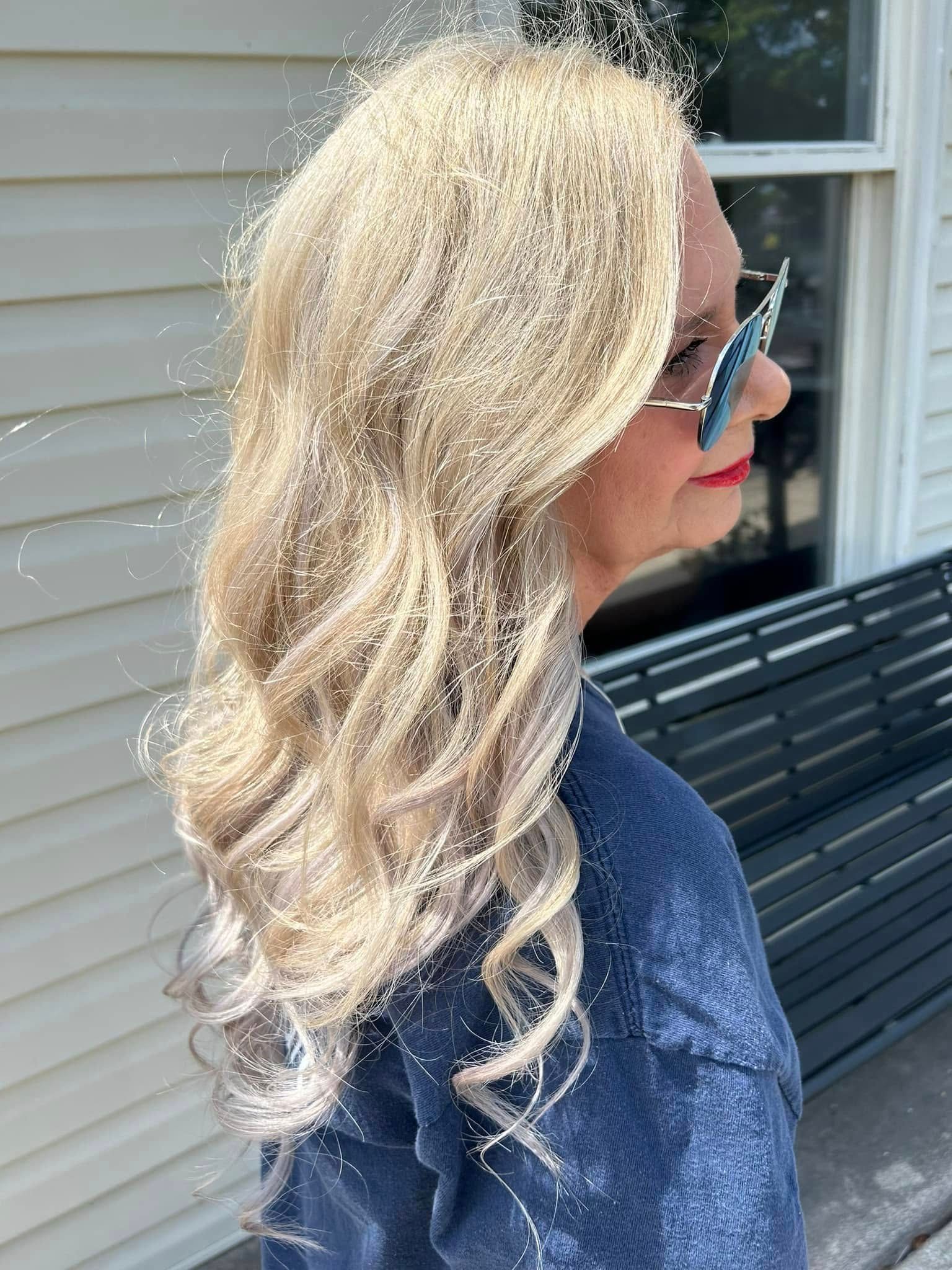 Woman in blue shirt with long wavy blonde hair and sunglasses outdoors.