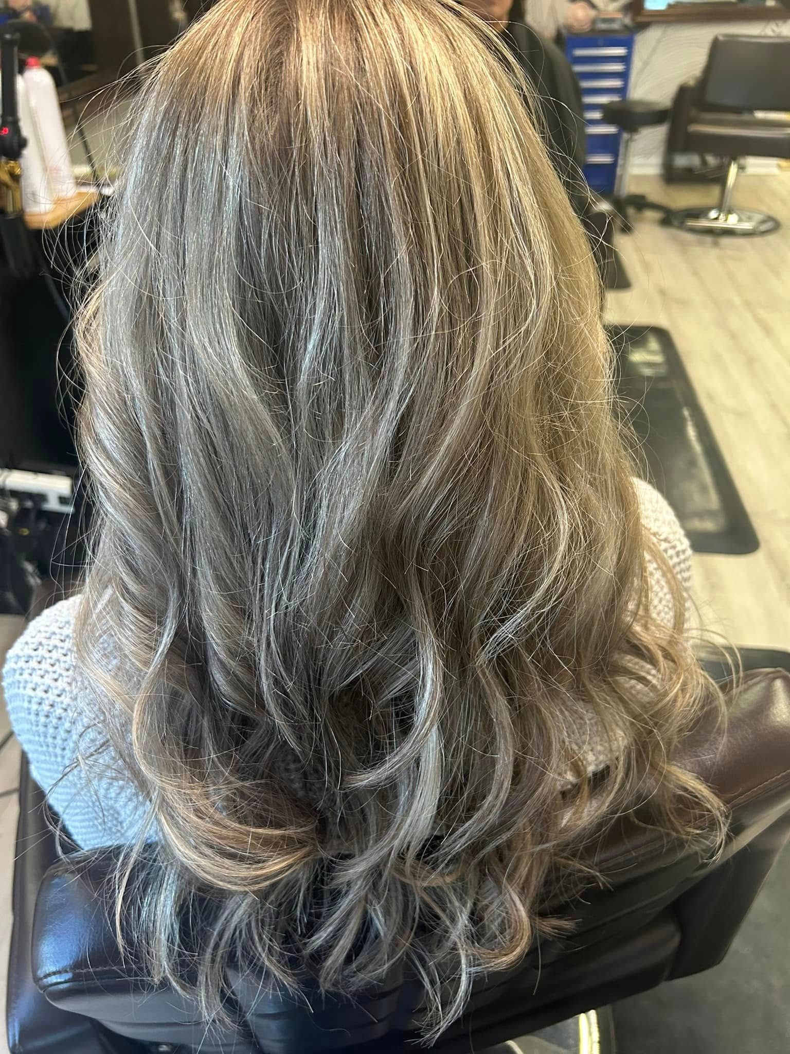 Person with wavy, light brown and blonde highlights sitting in a salon chair.