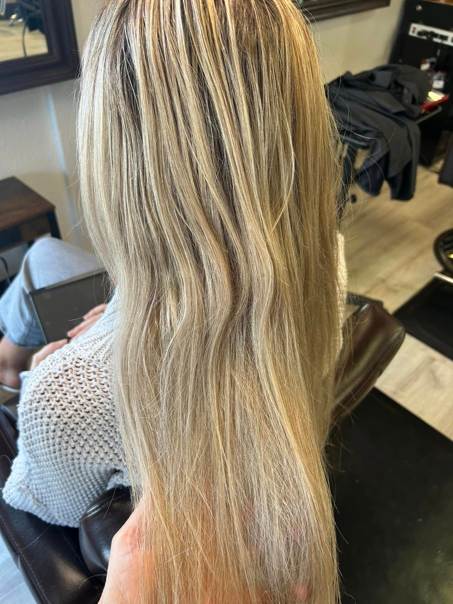 Blonde hair in a salon setting. A person is seated, facing away, with long, light-colored hair.