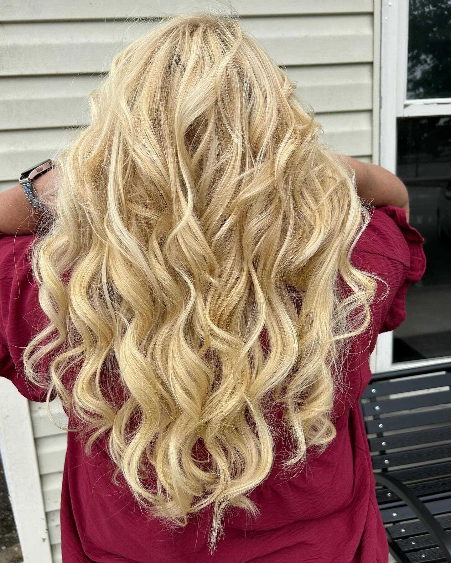 Long blonde wavy hair on a person wearing a maroon shirt, outdoors.
