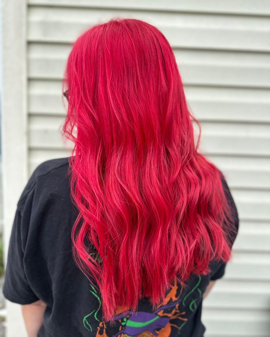 Person with long, wavy, bright red hair wearing a black t-shirt. Outdoor setting.