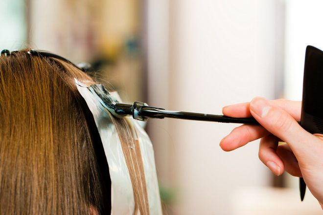 Hair dye being applied to brown hair with a brush and gloved hand