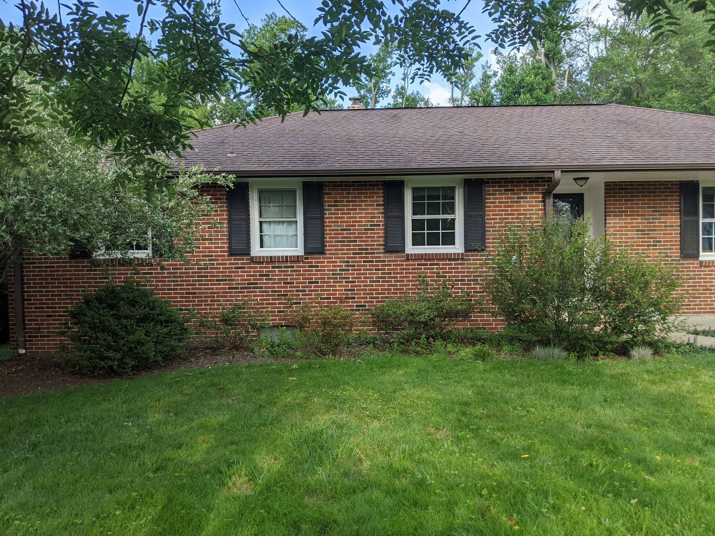 A brick house with black shutters and a lush green lawn in front of it.