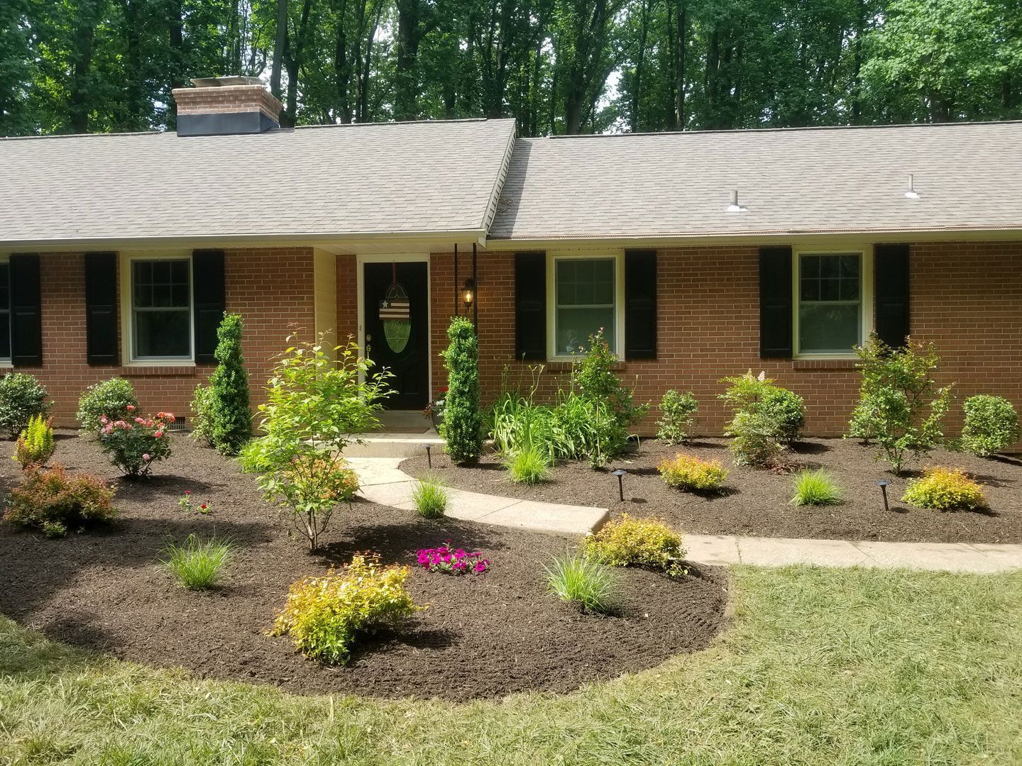 A brick house with black shutters and a walkway in front of it