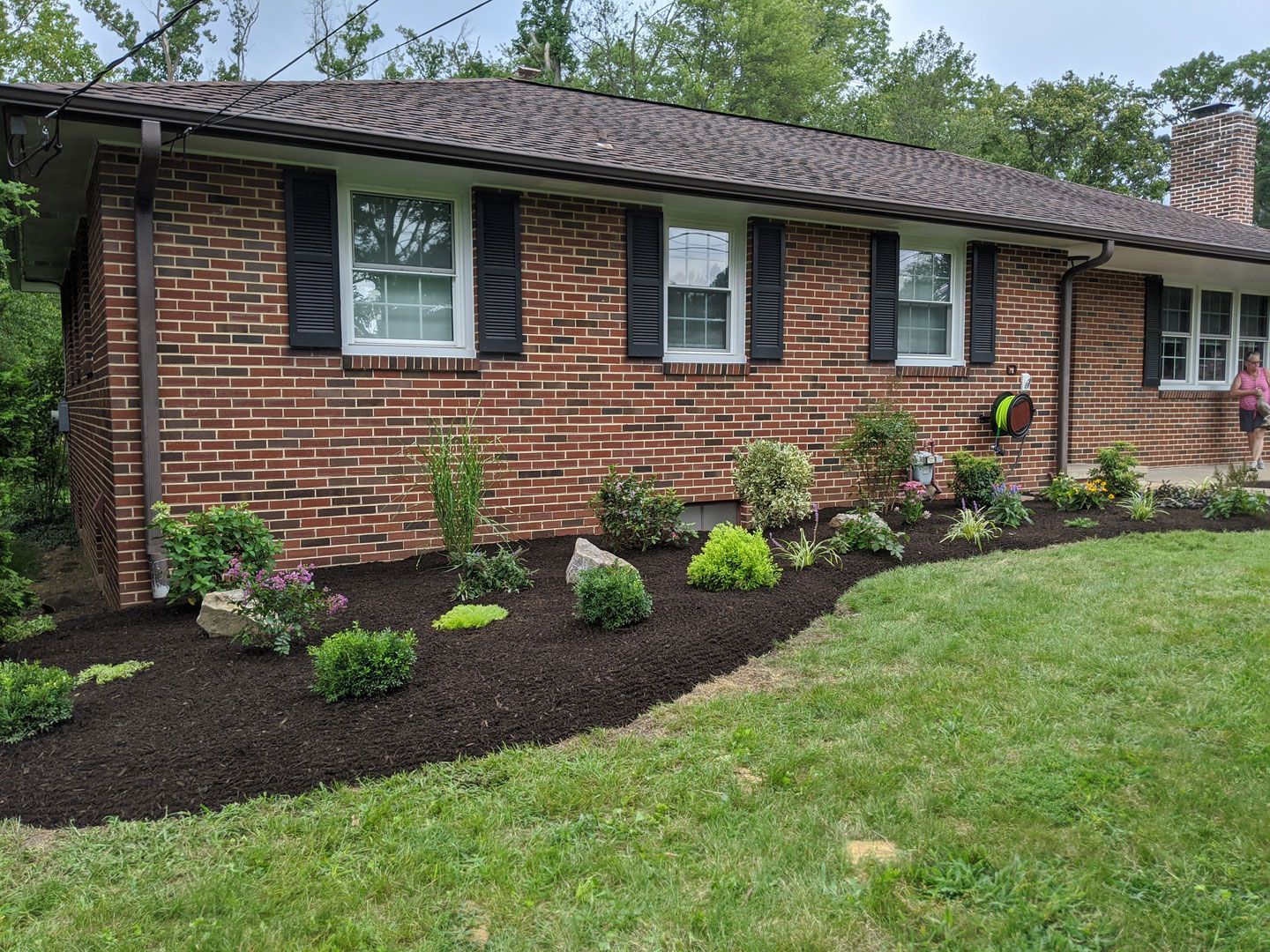 A brick house with black shutters and a lush green lawn in front of it.