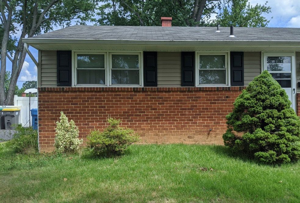 A brick house with black shutters and a tree in front of it.
