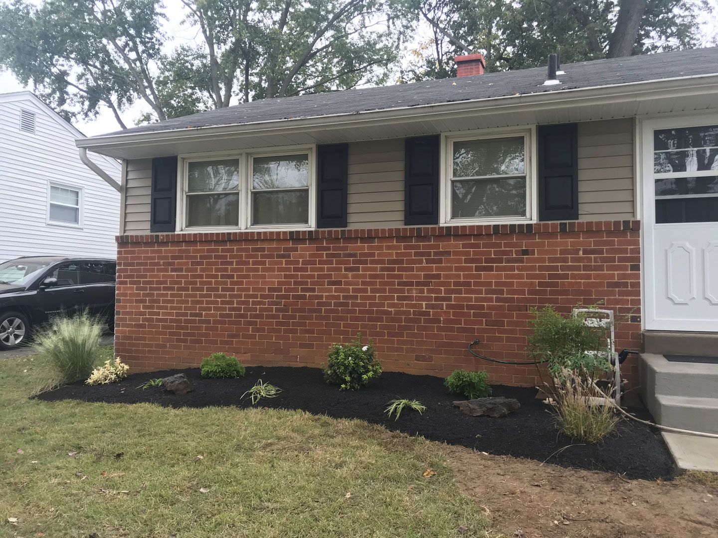 A brick house with black shutters and a car parked in front of it.