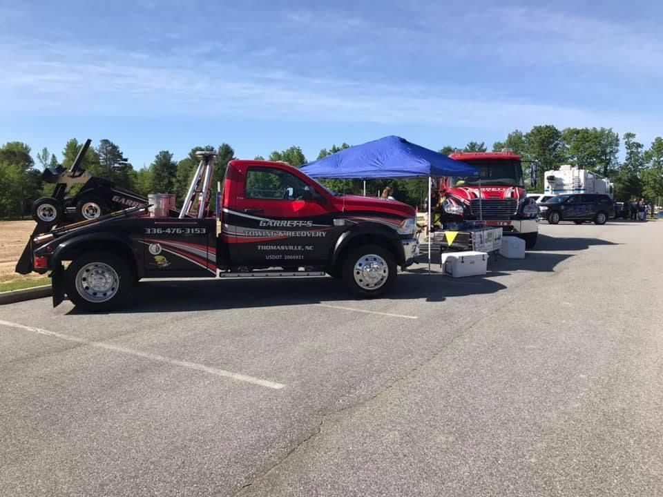 Tow trucks parked in a lot under a blue canopy on a sunny day.