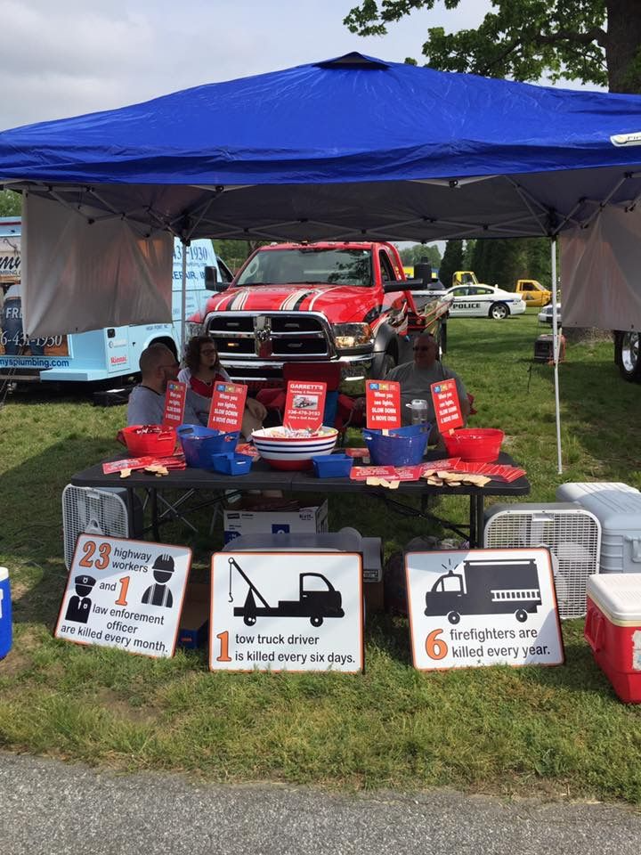 A safety booth at an outdoor event: people, red truck, signs with statistics on injuries from vehicles.