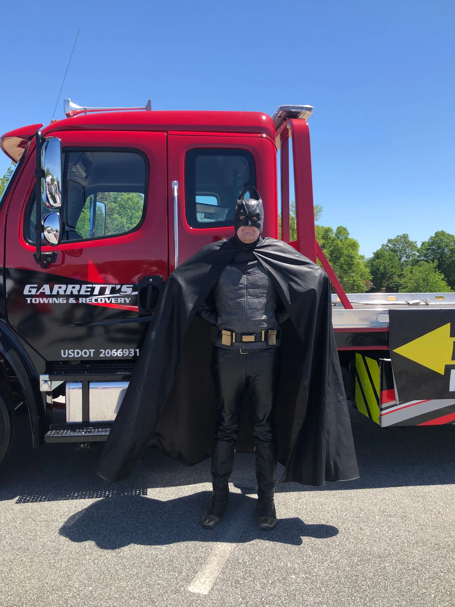 Batman poses in front of a red tow truck.