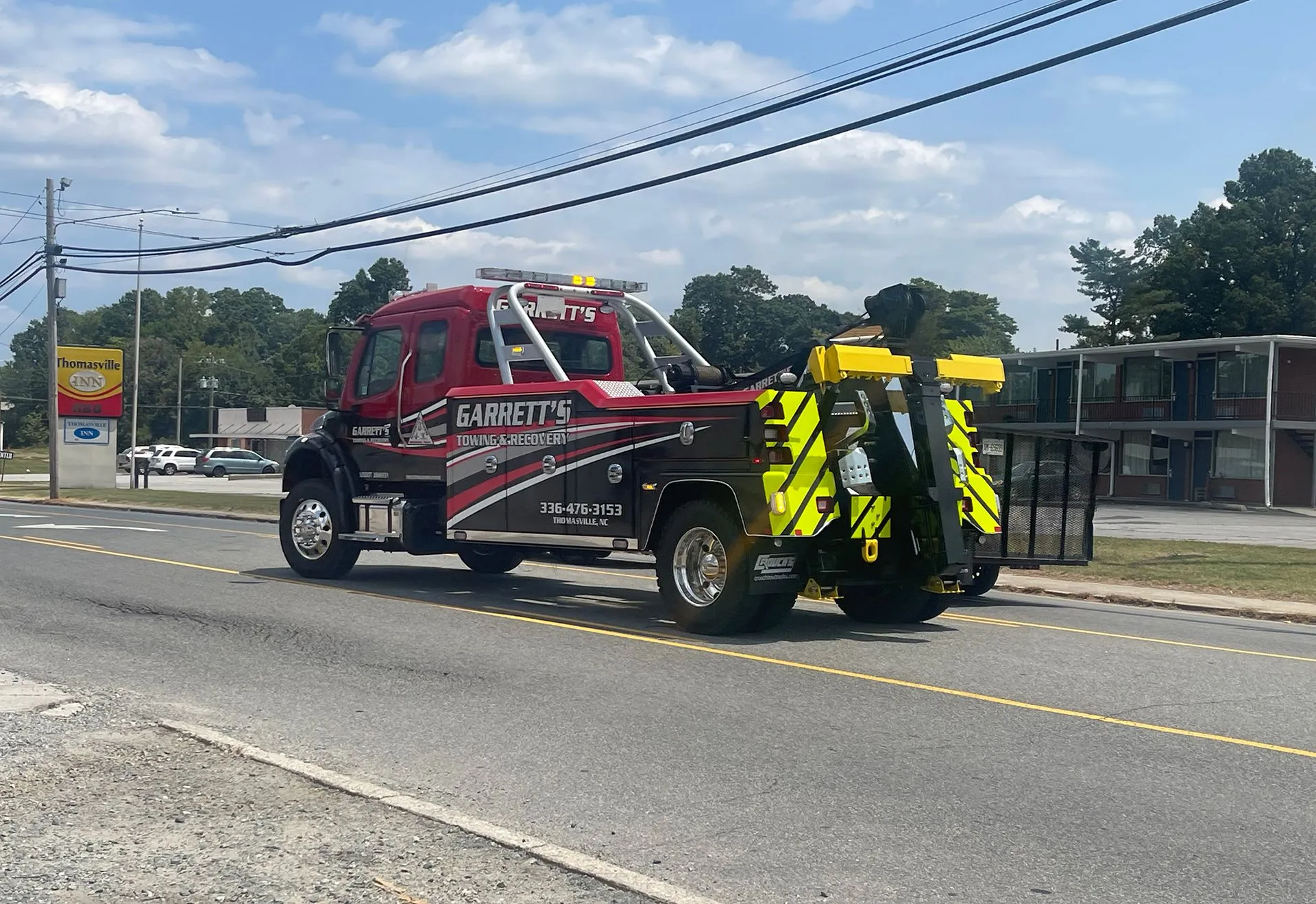 Red and black tow truck on a road, parked in front of a building, sunny day.
