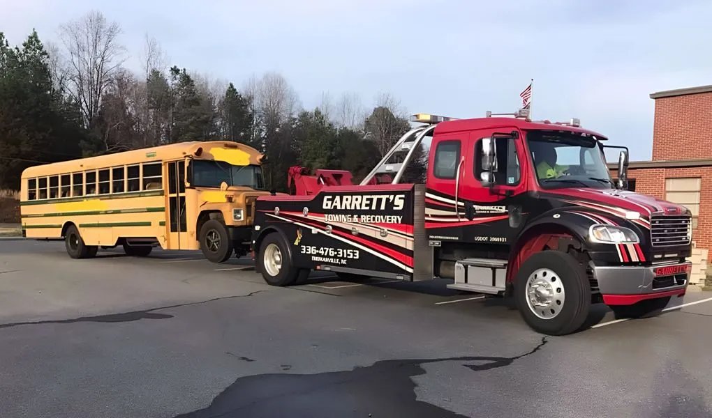 A yellow school bus being towed by a red and black tow truck in a parking lot.